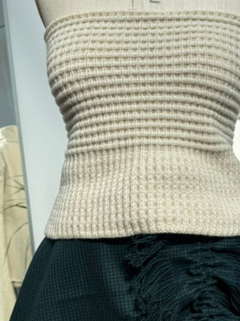 A mannequin torso wearing a cream ribbed knit strapless top paired with a dark teal ruffled skirt, photographed inside a clothing studio