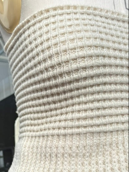 A close-up of a cream-colored ribbed knit waist corset attached to a dress form, with a dark teal skirt below.