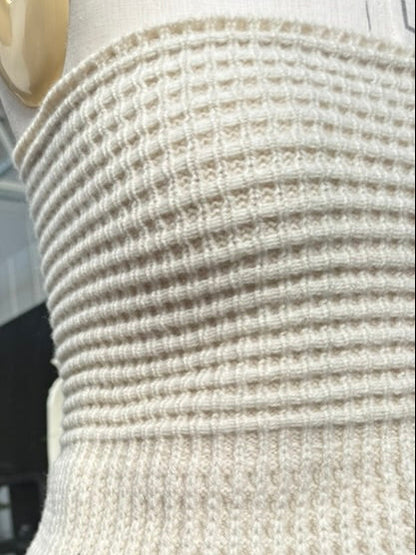 A close-up of a cream-colored ribbed knit waist corset attached to a dress form, with a dark teal skirt below.